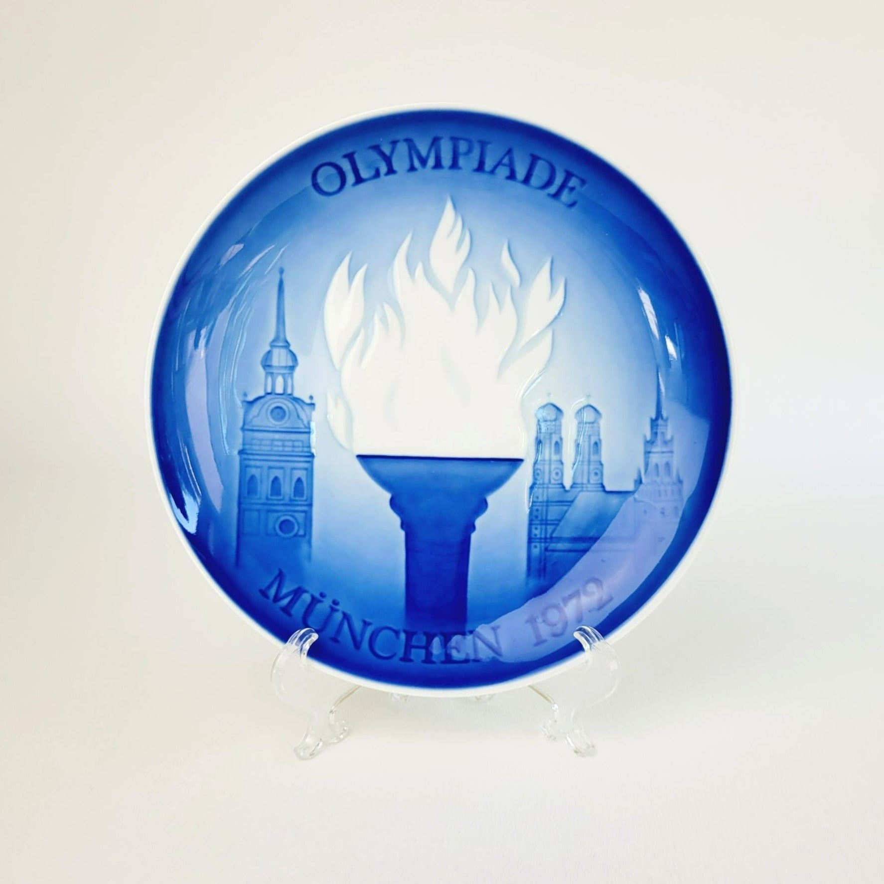 A blue and white Royal Copenhagen porcelain plate with 'Olympiade München 1972' design featuring Olympic torch and iconic buildings.