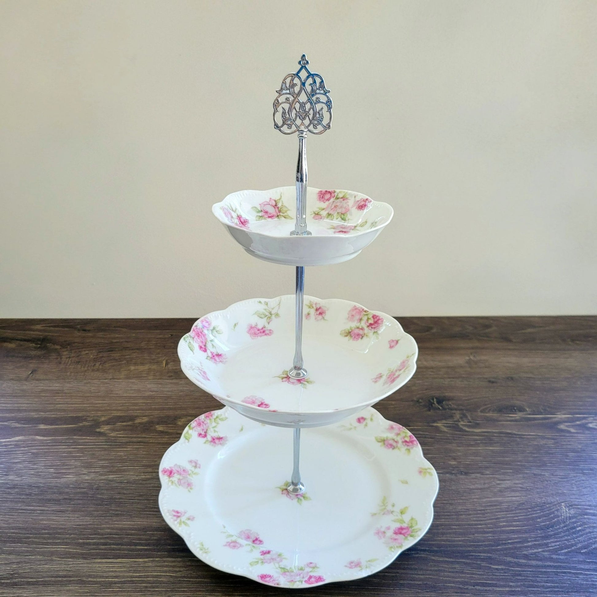 Three-tiered ceramic cake stand with floral design on a wooden surface.