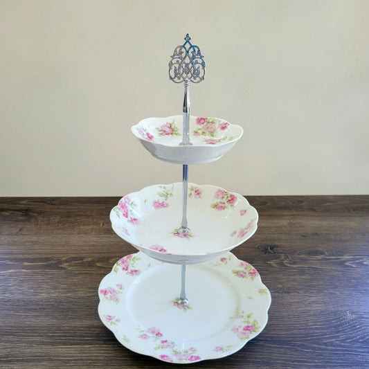 Three-tiered ceramic cake stand with floral design on a wooden surface.